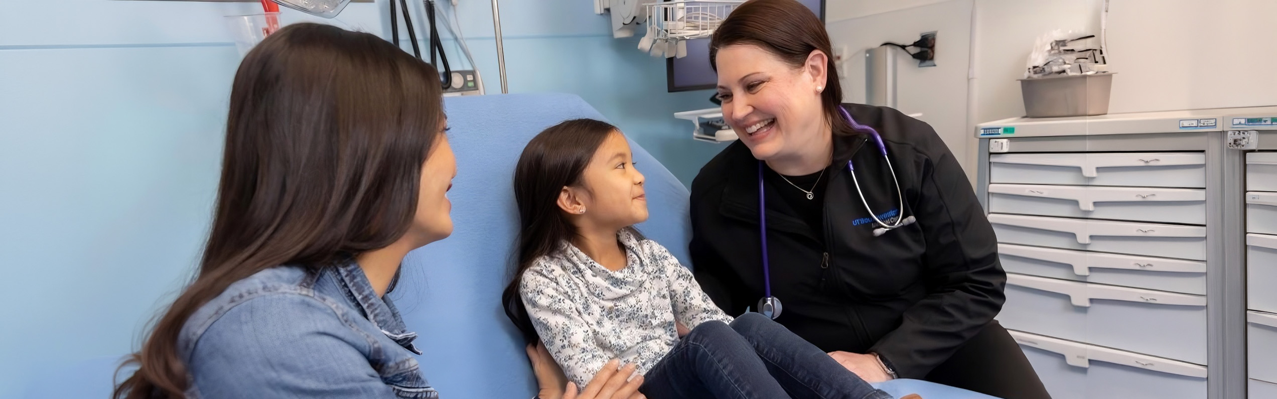 A doctor talking to a young girl patient with her mother next to her.
