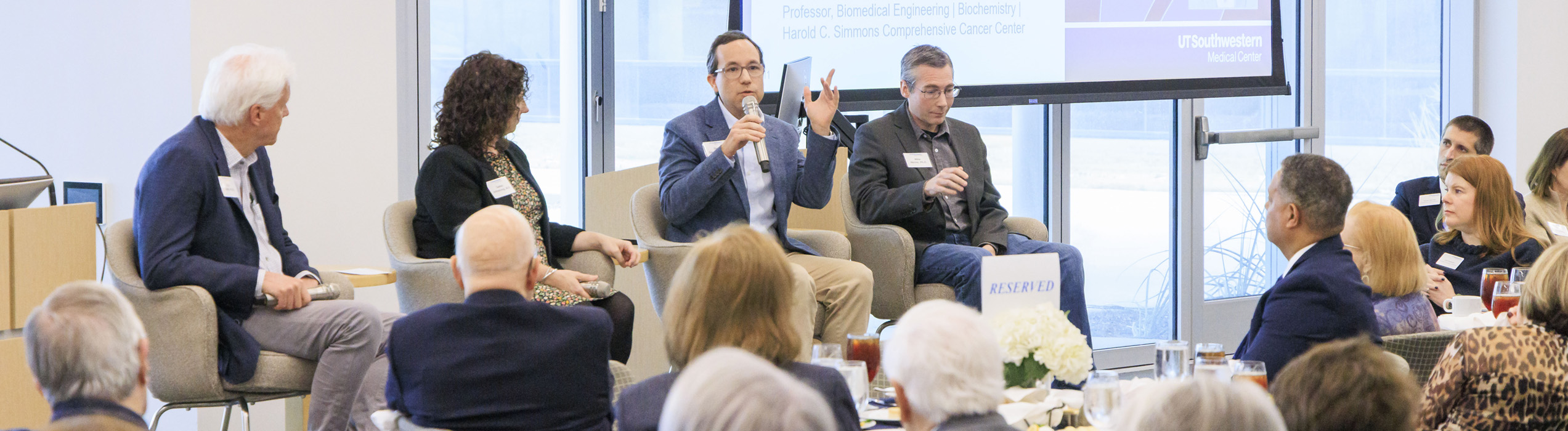 Panelists participate in a discussion during a UT Southwestern event as attendees listen from banquet tables.