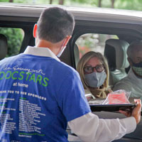 An event volunteer delivers science kits on a tray to guests waiting in their car