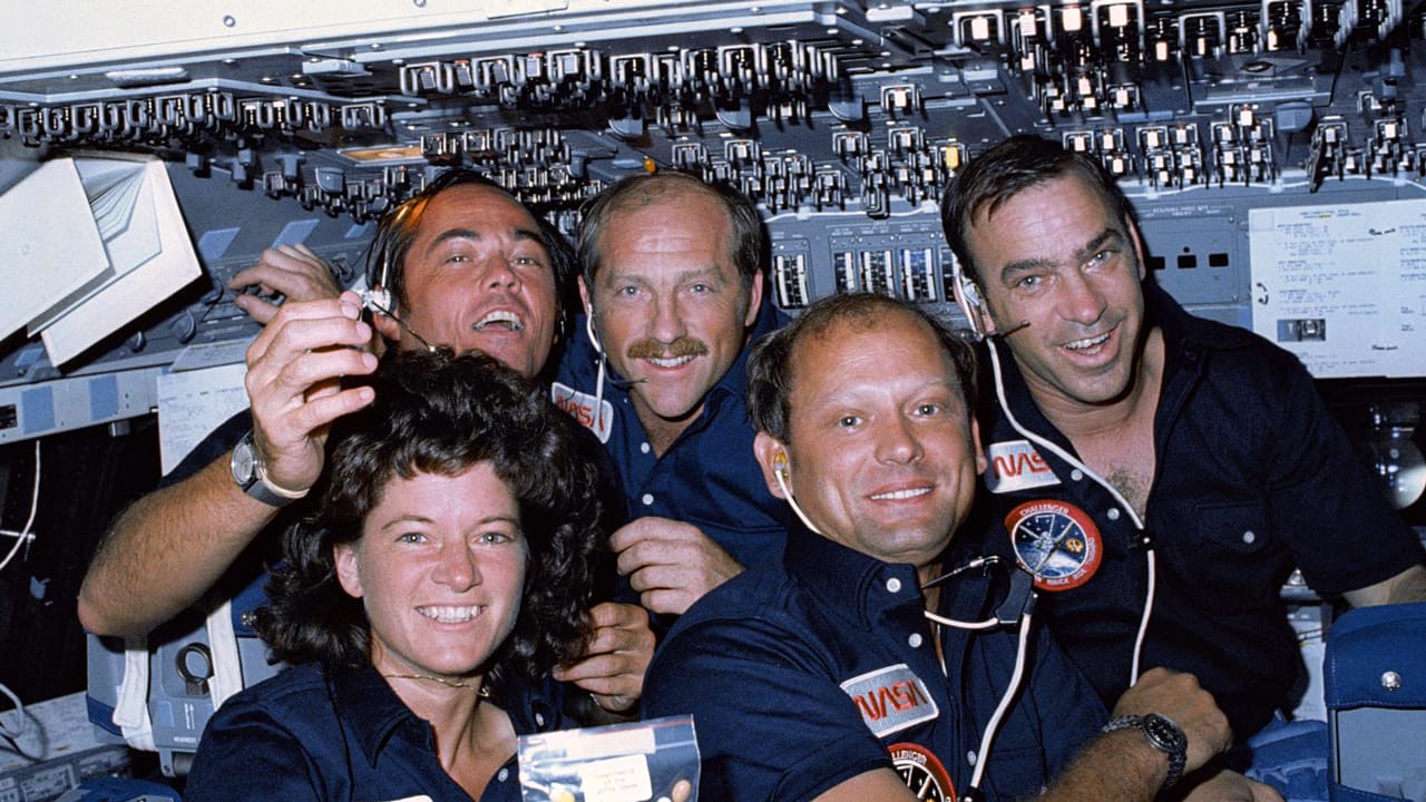 Astronauts Sally Ride, Robert Crippen, Frederick Hauck, Norman Thagard, and John Fabian pose for a group photo on the flight deck of the Space Shuttle Challenger with a bag of jelly beans.