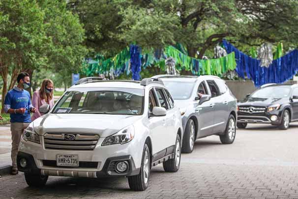 A line of cars drive onto the UT Southwestern campus past trees decorated with colorful streamers