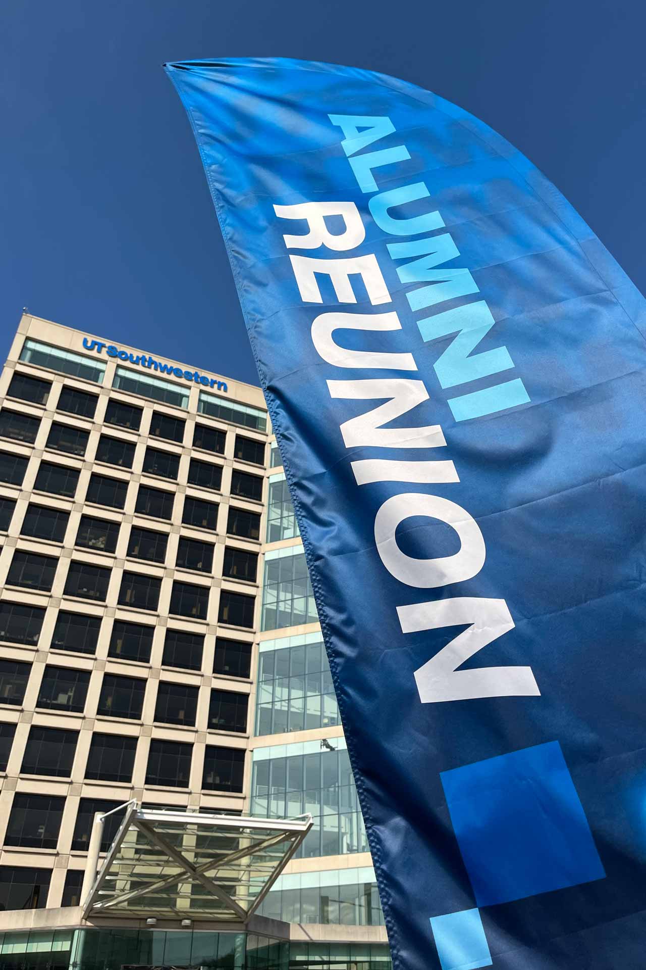 A blue banner with the words Alumni Reunion stands in front of a 14-story building. Across the top of the building is a sign that reads 'UT Southwestern.'