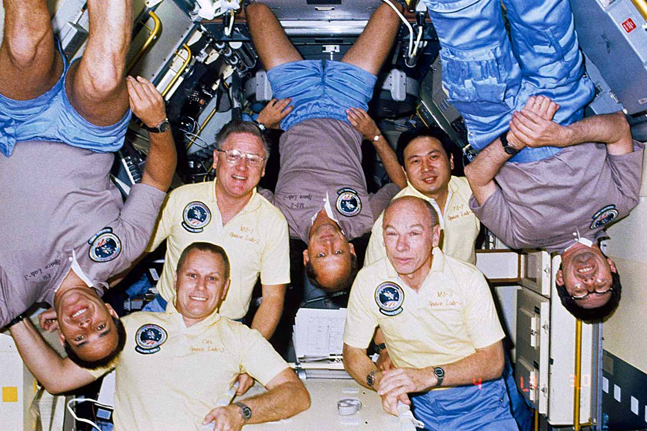 Astronauts Frederick Gregory, Robert Overmyer, Don Lind, Norman Thagard, William E. Thornton, Taylor Wang, and Lodewijk van den Berg pose for a group photo inside the Long Science Module for Spacelab 3 located in the cargo bay of the Space Shuttle Challenger.