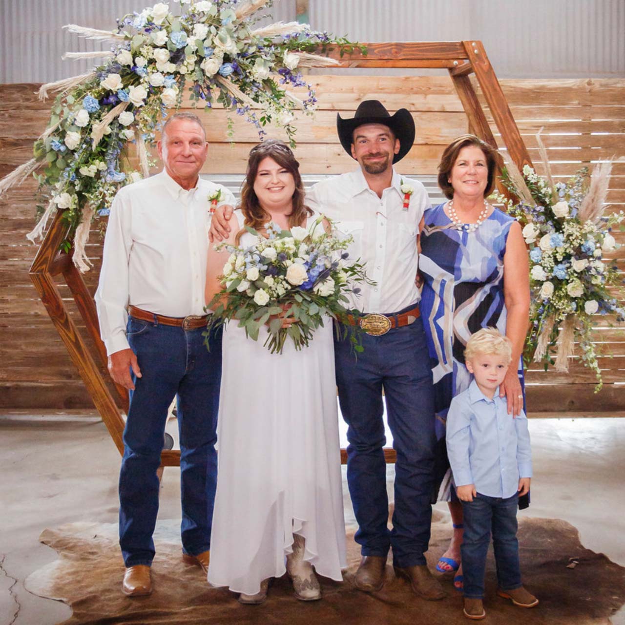 A group photo of the Crofoot family standing under a floral arch on the day of their son's wedding. Beneath their feet is a cowhide.