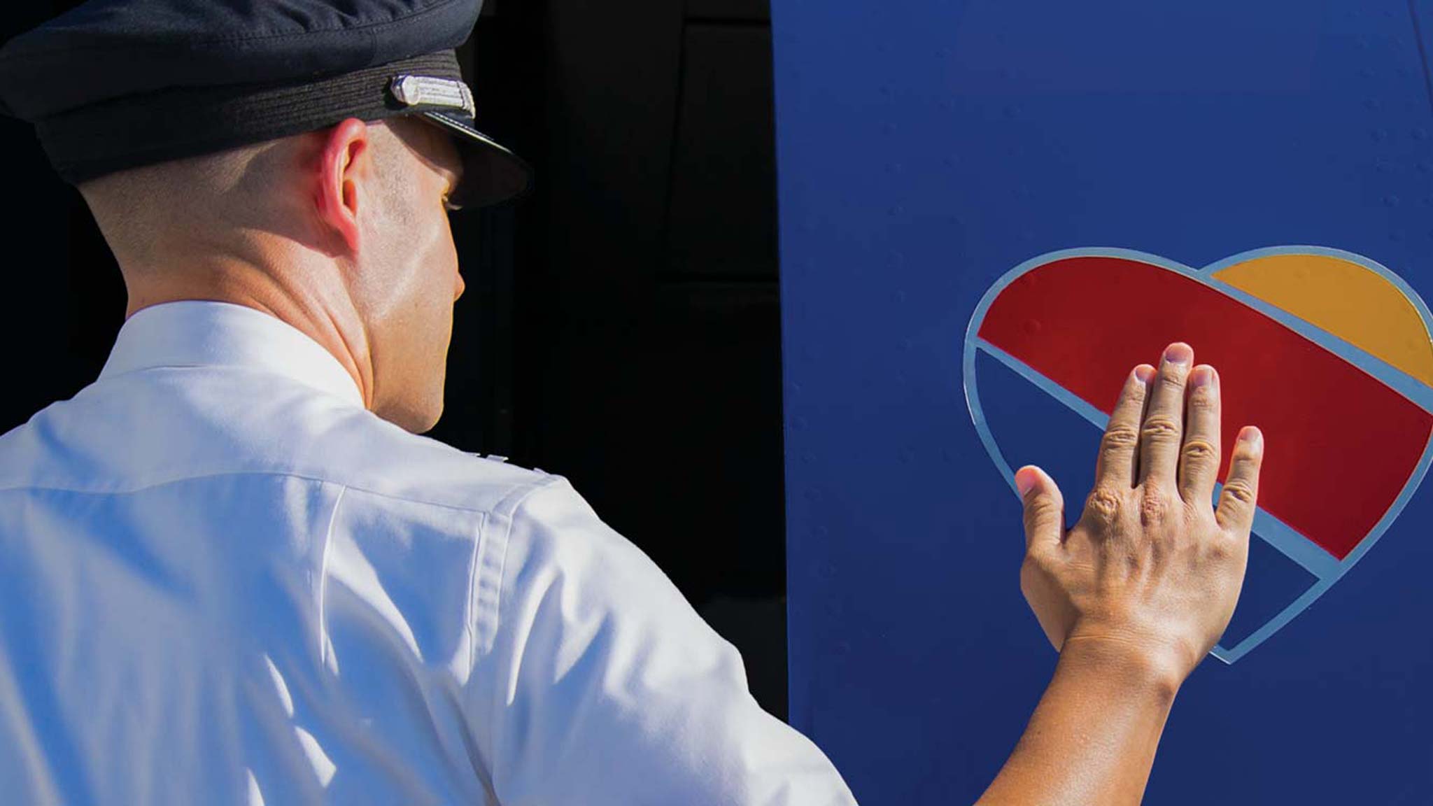 A Southwest Airlines pilot touches the company's heart shaped logo painted on the side of an airplane as he steps through the craft's door.