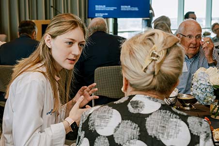 A medical school student seated at a table speaks with an alumnae during a lunch event.