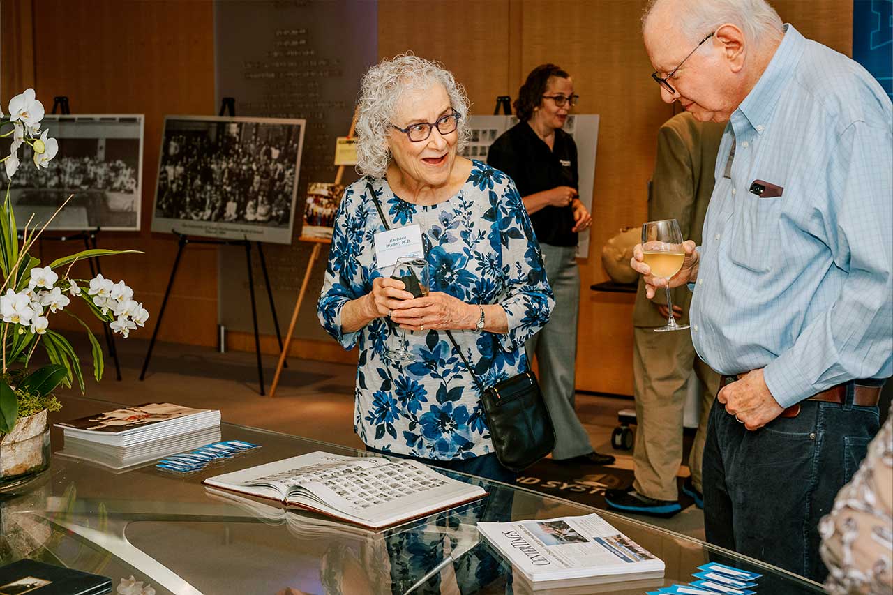 A man and a woman speak to each other while looking at an open book placed on a table.