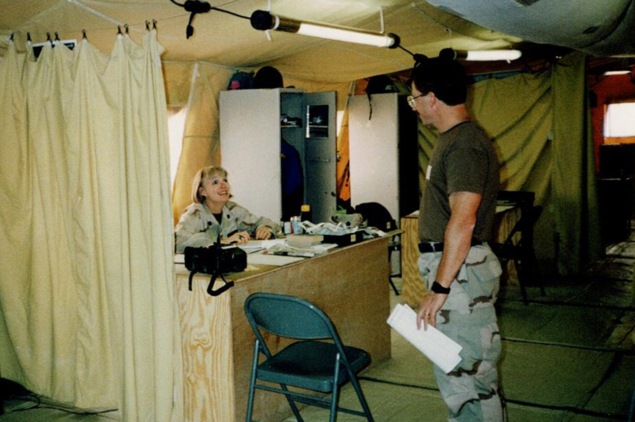 Gladys Young sitting at a desk in a field hospital, talking to a standing man.