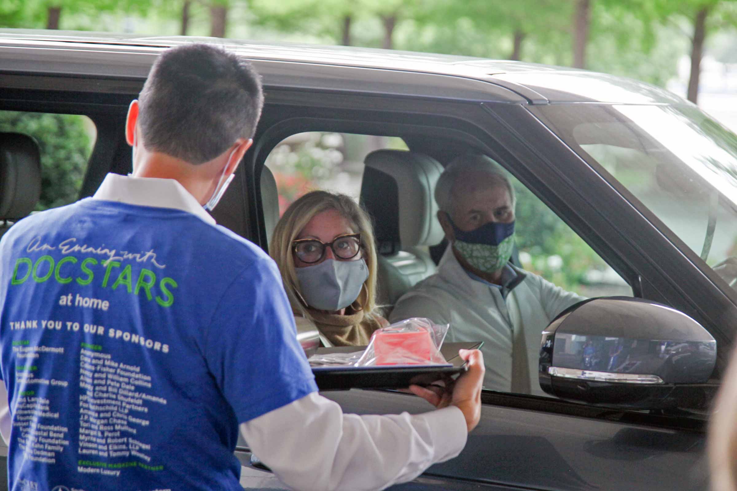 An event volunter carries science experiments on a tray to event guests waiting in their vehicle.