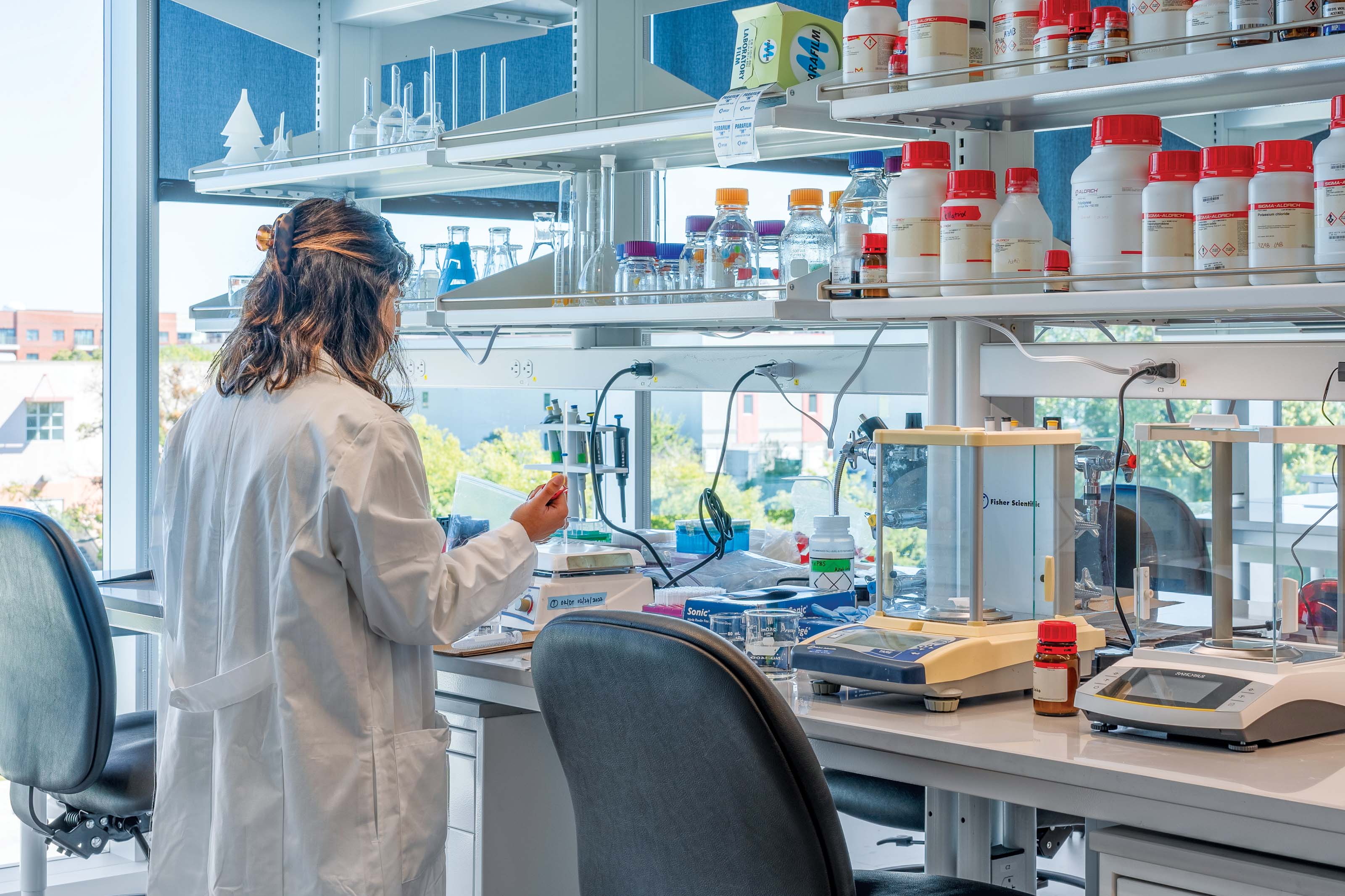 A research scientist next to a large desk of small testing materials and equipment.