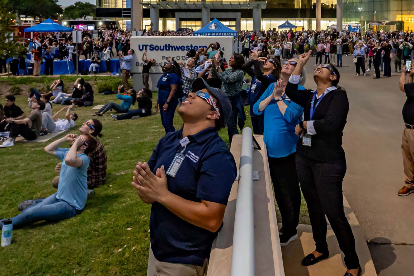 UT Southwestern staff and students wear eclipse goggles and view the exlipse outside Peter O'Donnell Jr. Biomedical Research Building.